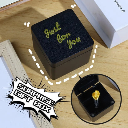 Black gift box with 'Just for you' text on a wooden surface, featuring a small gold figurine.