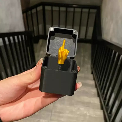 Black electronic device with a gold middle finger figure held by a hand.