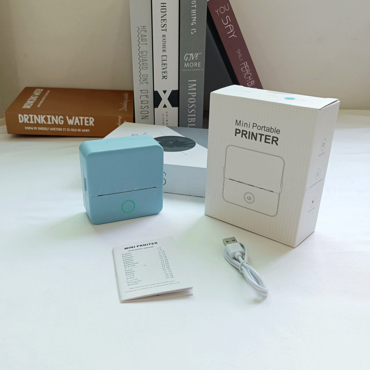 Mini portable printer with packaging, user manual, and USB cable on a white surface.