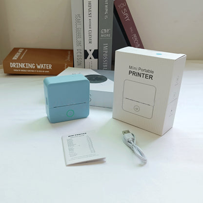 Mini portable printer with packaging, user manual, and USB cable on a white surface.