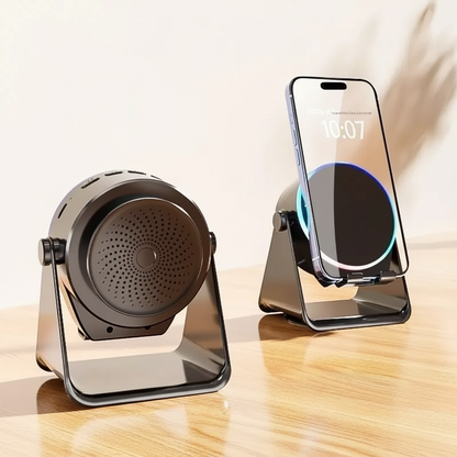 A black and gray magnetic wireless charging stand shown in two views on a wooden table against a light beige wall. One view shows the stand empty, and the other shows a smartphone placed upright inside the charging cradle with a wireless charging indicator visible.